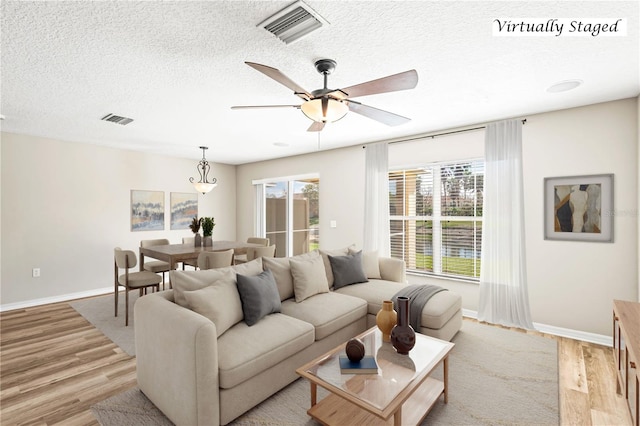 living area featuring baseboards, light wood-style flooring, visible vents, and a textured ceiling