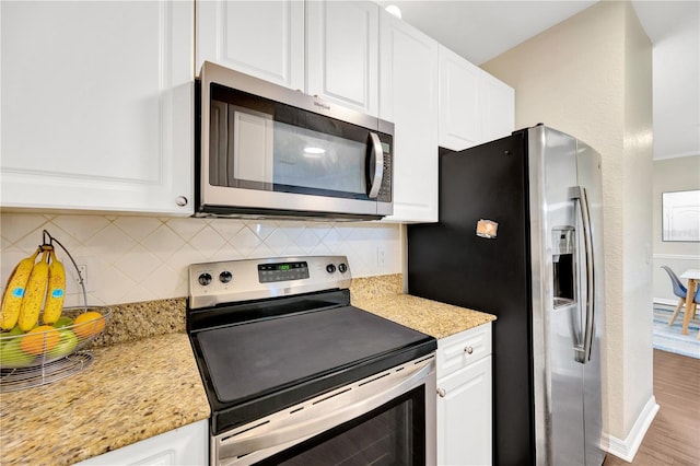 kitchen with white cabinets, appliances with stainless steel finishes, light stone counters, wood finished floors, and backsplash