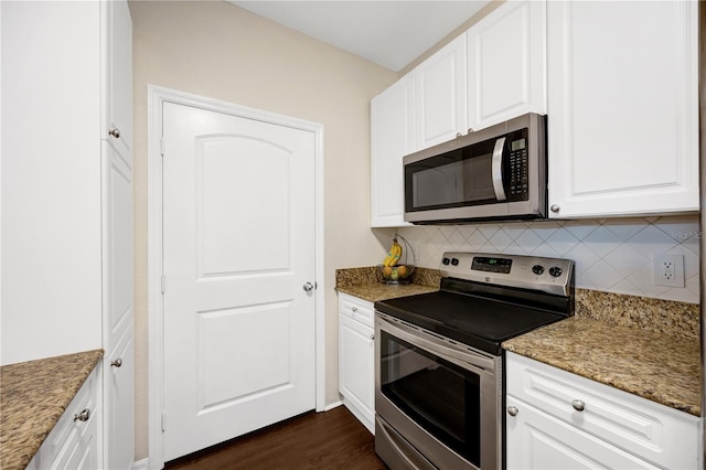 kitchen with dark wood-style floors, tasteful backsplash, appliances with stainless steel finishes, white cabinets, and dark stone counters