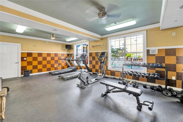 gym with a wainscoted wall, ceiling fan, visible vents, and a raised ceiling