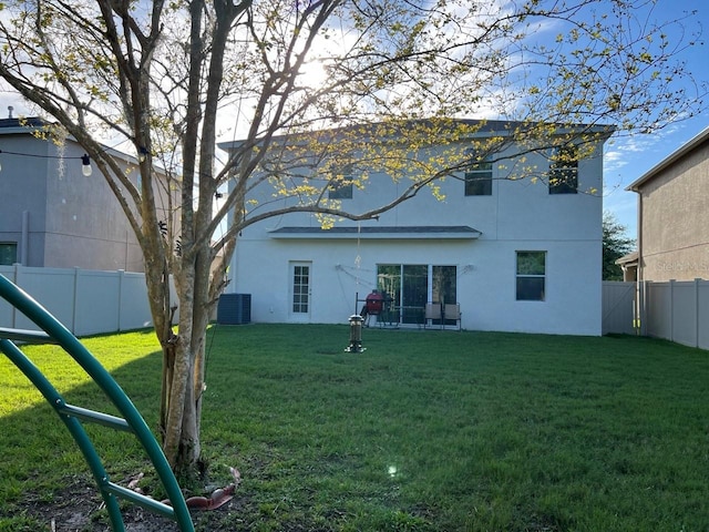 back of house with central AC, a lawn, a fenced backyard, and stucco siding