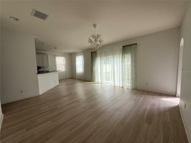 unfurnished living room featuring arched walkways, a sink, wood finished floors, visible vents, and baseboards