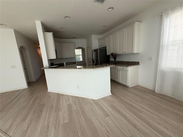 kitchen featuring light wood-style floors, arched walkways, dark stone countertops, and black fridge with ice dispenser