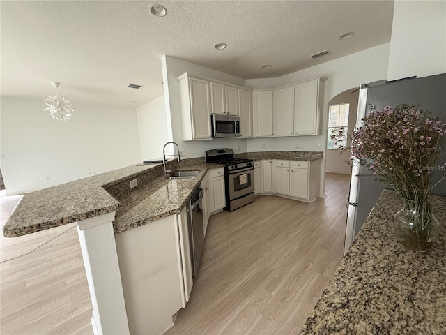 kitchen featuring stone counters, stainless steel appliances, a peninsula, a sink, and light wood-style floors