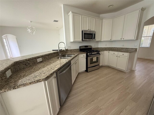 kitchen with arched walkways, appliances with stainless steel finishes, dark stone countertops, light wood-type flooring, and a sink