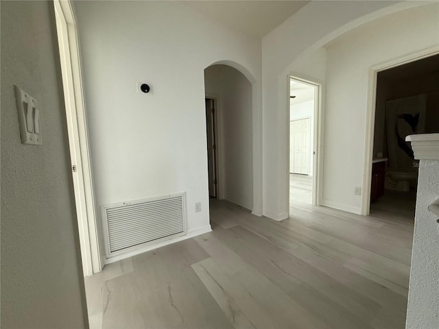 empty room with arched walkways, wood finished floors, visible vents, and baseboards