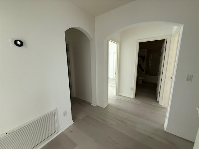 hallway with baseboards, visible vents, arched walkways, and wood finished floors