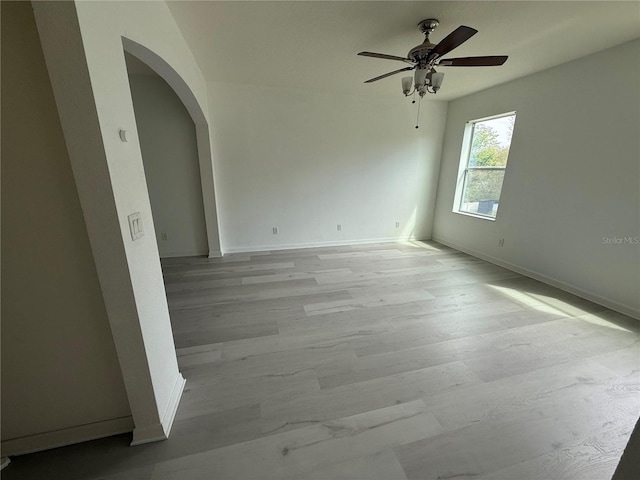 unfurnished room featuring arched walkways, ceiling fan, wood finished floors, and baseboards