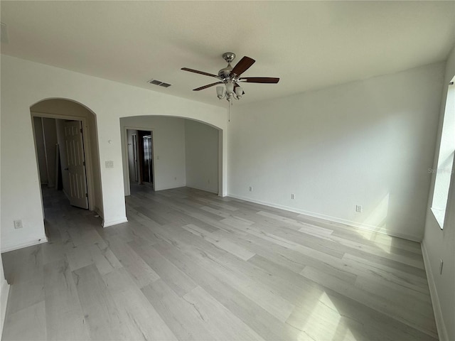 unfurnished room with visible vents, arched walkways, baseboards, ceiling fan, and light wood-type flooring