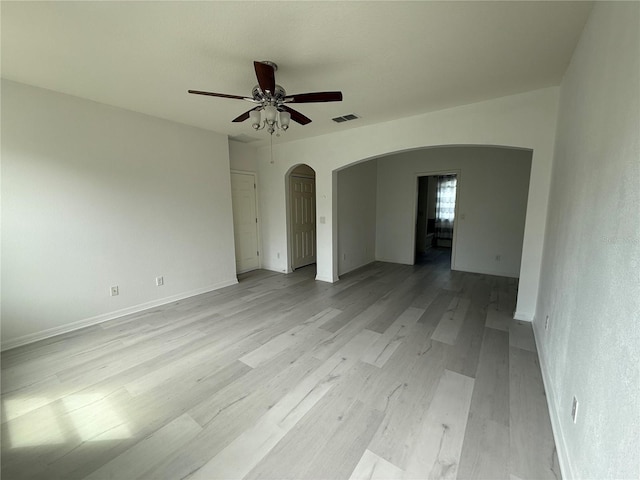 empty room featuring arched walkways, light wood finished floors, visible vents, ceiling fan, and baseboards