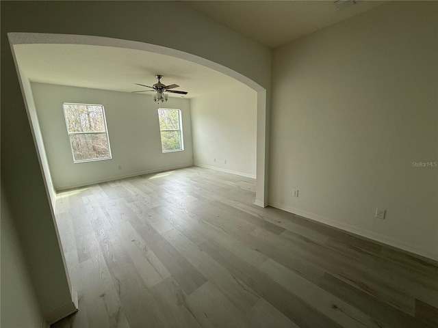 unfurnished room with baseboards, ceiling fan, arched walkways, and wood finished floors