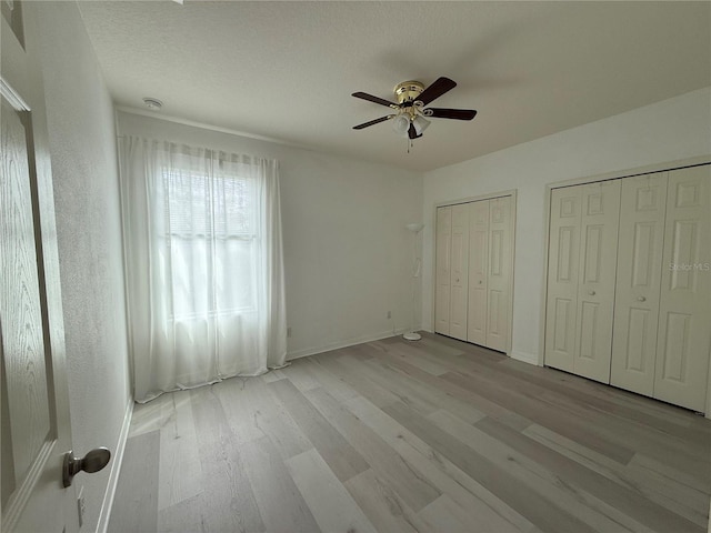 unfurnished bedroom with multiple closets, ceiling fan, baseboards, and wood finished floors