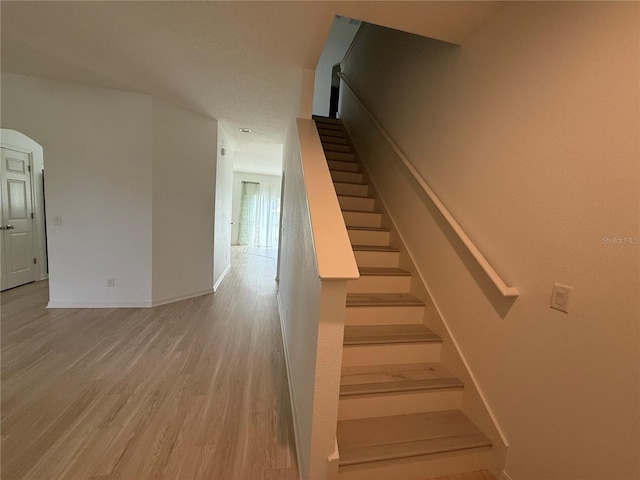 stairway featuring baseboards, arched walkways, and wood finished floors