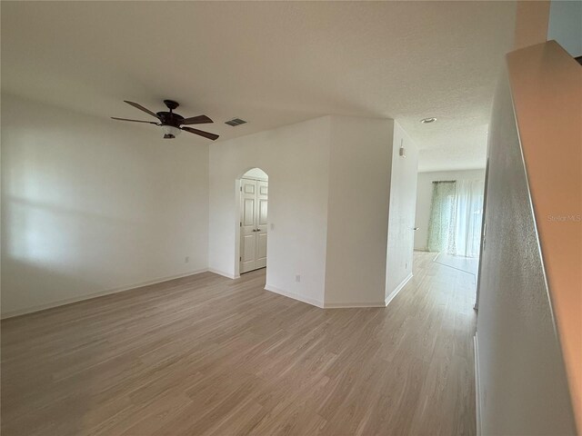 empty room with arched walkways, ceiling fan, visible vents, baseboards, and light wood finished floors