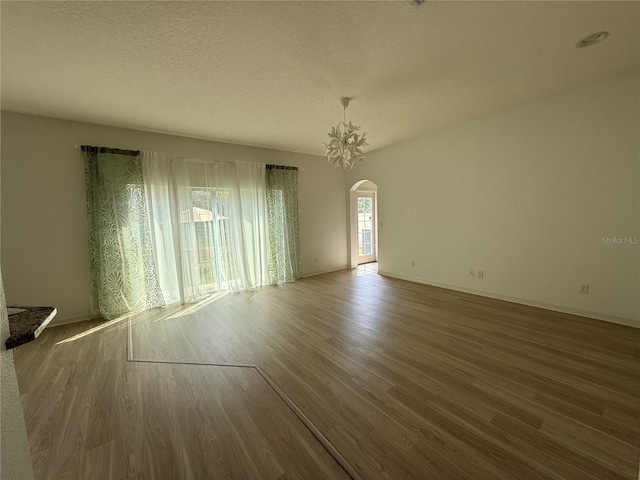 unfurnished room with arched walkways, a textured ceiling, wood finished floors, and baseboards