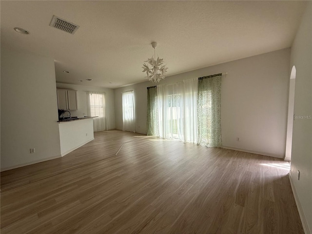 unfurnished living room featuring baseboards, visible vents, arched walkways, wood finished floors, and a sink