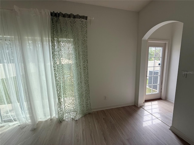 empty room with baseboards, arched walkways, and wood finished floors