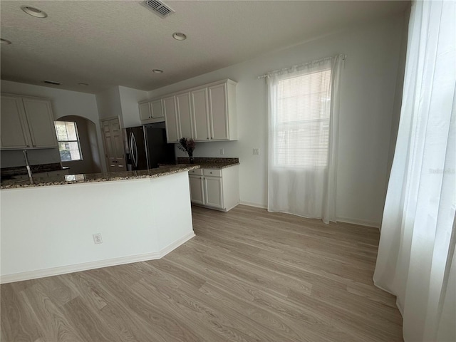 kitchen featuring visible vents, arched walkways, black fridge with ice dispenser, dark stone countertops, and light wood-style floors