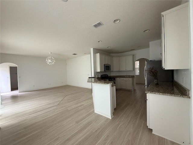 kitchen featuring visible vents, white cabinets, arched walkways, appliances with stainless steel finishes, and open floor plan