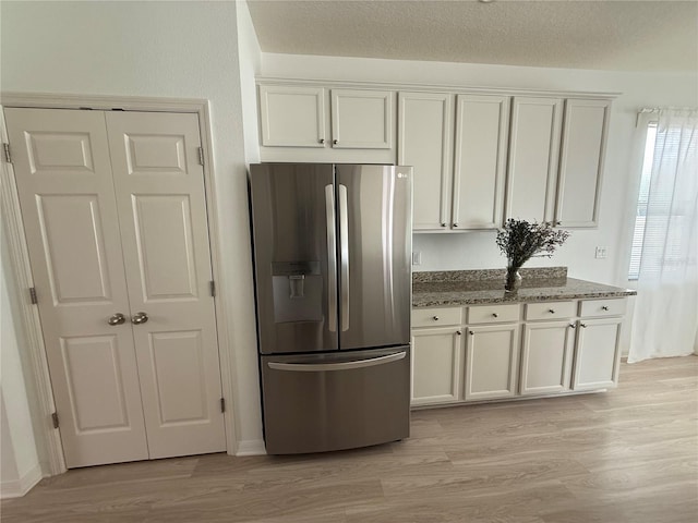 kitchen with dark stone counters, a textured ceiling, stainless steel refrigerator with ice dispenser, and light wood-style floors