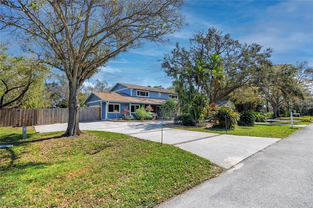 view of front facade featuring concrete driveway, a front yard, and fence