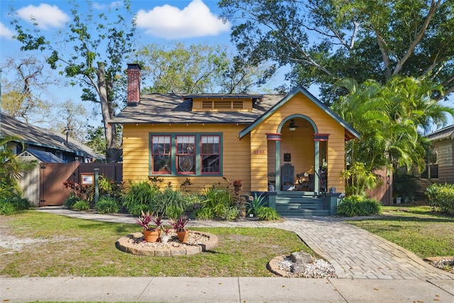 bungalow-style house featuring a front lawn, a chimney, and fence