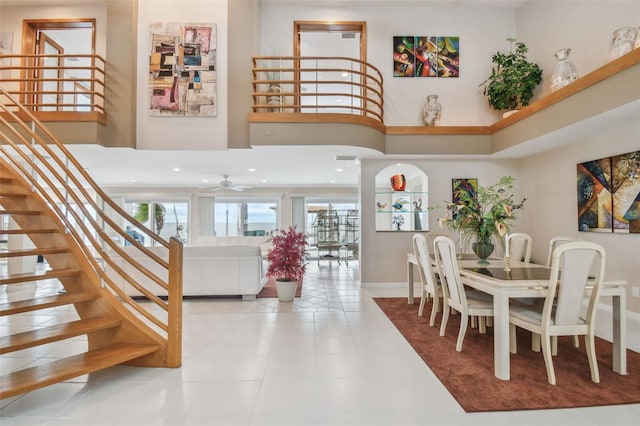 dining space featuring a high ceiling, a ceiling fan, tile patterned flooring, baseboards, and stairs