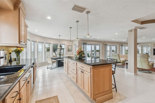 kitchen with tasteful backsplash, visible vents, a breakfast bar area, a center island, and light brown cabinetry