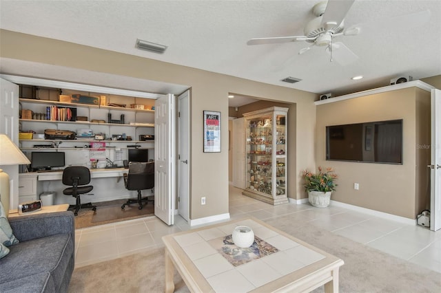 tiled living area featuring a textured ceiling, carpet floors, visible vents, baseboards, and a ceiling fan