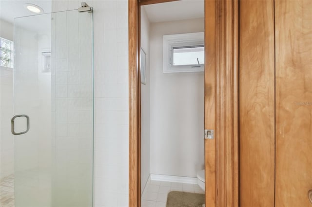 bathroom featuring baseboards, a healthy amount of sunlight, a shower stall, and toilet