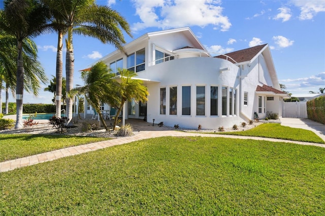 art deco house with a front yard, an outdoor pool, fence, and stucco siding