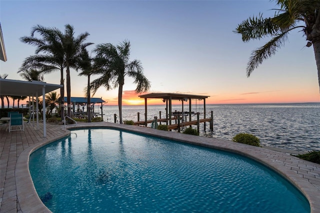 pool at dusk with an outdoor pool, a patio, a boat dock, boat lift, and a water view