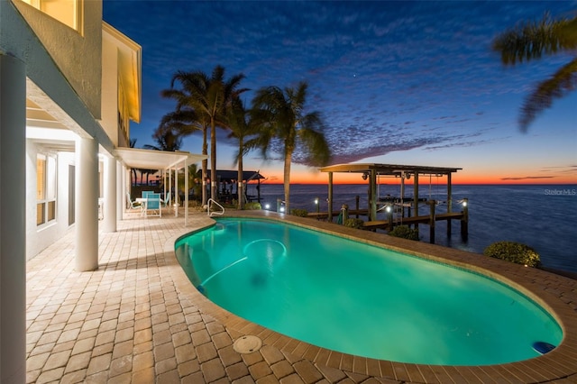 pool at dusk with an outdoor pool, a patio, boat lift, a dock, and a water view