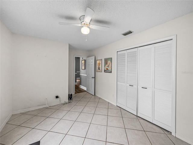 unfurnished bedroom with light tile patterned floors, ceiling fan, a textured ceiling, visible vents, and a closet