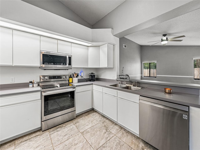 kitchen with stainless steel appliances, lofted ceiling, white cabinetry, a sink, and a textured ceiling