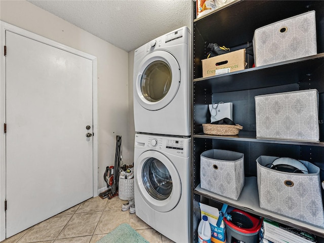 clothes washing area with stacked washer and dryer, tile patterned flooring, laundry area, and a textured ceiling