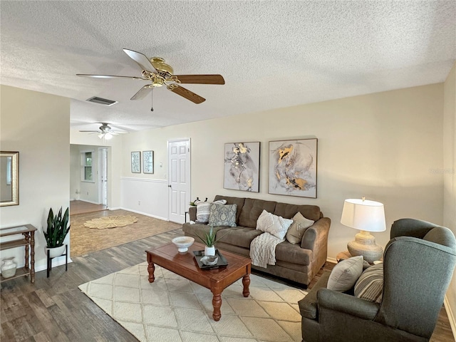 living room featuring a textured ceiling, ceiling fan, wood finished floors, and visible vents