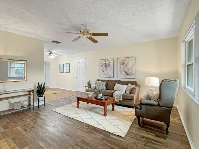 living room with visible vents, light wood-style flooring, ceiling fan, a textured ceiling, and baseboards