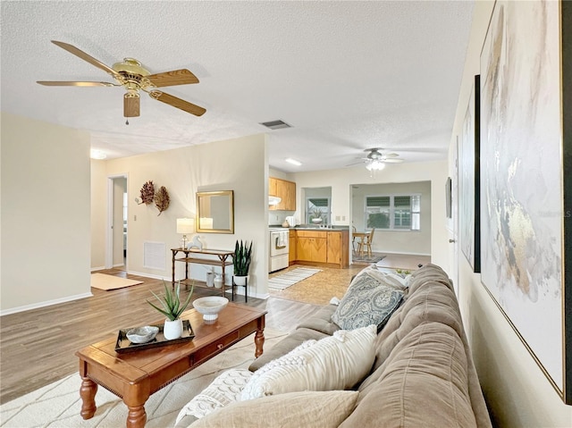 living room featuring a textured ceiling, light wood-type flooring, visible vents, and baseboards