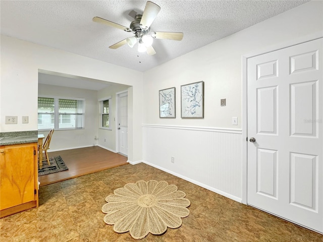 unfurnished office with a ceiling fan, a wainscoted wall, and a textured ceiling