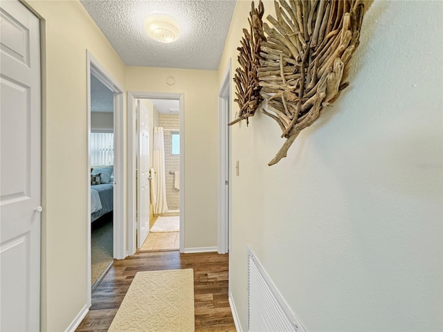 hallway with baseboards, a textured ceiling, visible vents, and wood finished floors