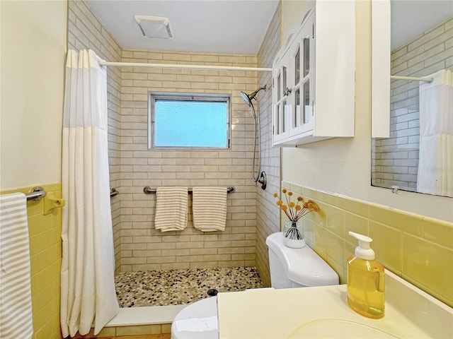 bathroom featuring tile walls, toilet, a stall shower, wainscoting, and vanity