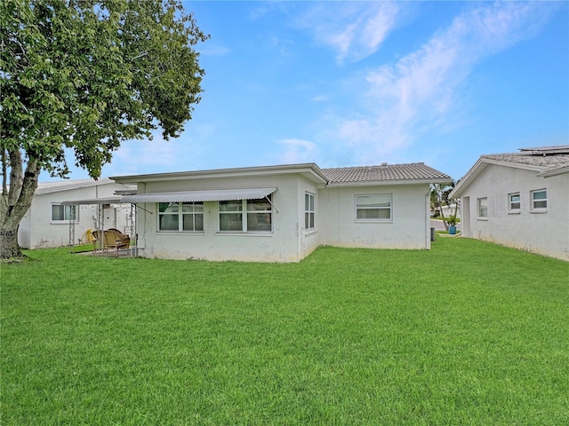 rear view of house with a yard, a tiled roof, and stucco siding