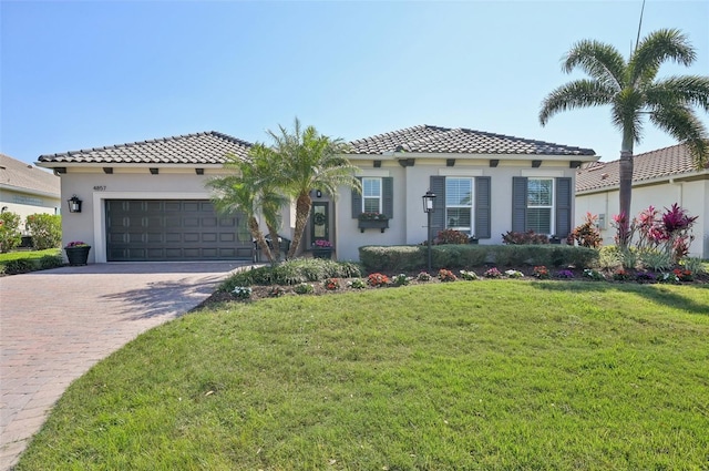 mediterranean / spanish-style house featuring decorative driveway, stucco siding, a garage, a tiled roof, and a front lawn