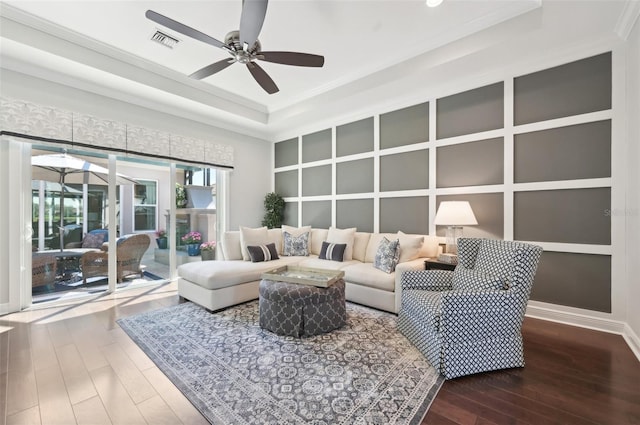 living room featuring a tray ceiling, visible vents, ornamental molding, ceiling fan, and wood finished floors