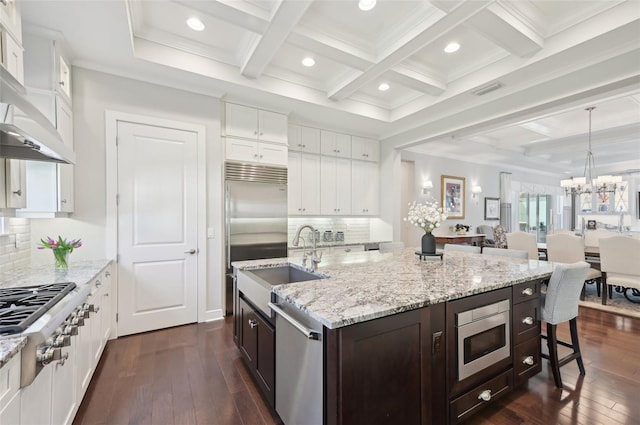 kitchen with appliances with stainless steel finishes, white cabinetry, a sink, wall chimney range hood, and dark brown cabinetry