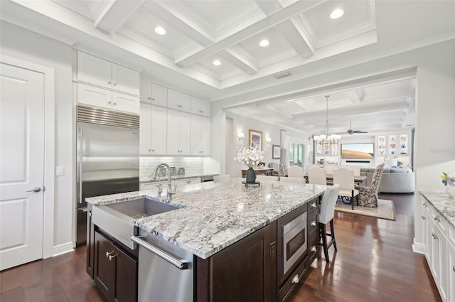 kitchen with dark brown cabinetry, white cabinets, dark wood-style flooring, built in appliances, and a sink