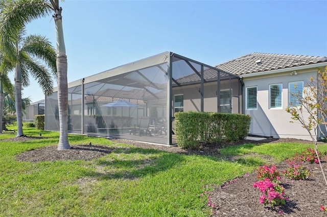 rear view of house with a yard, a tile roof, glass enclosure, and stucco siding