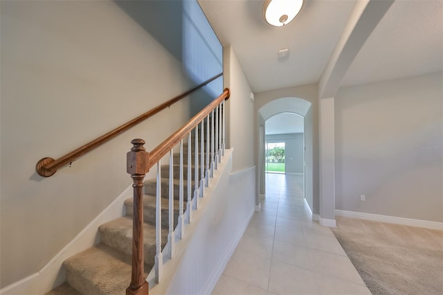 stairs with carpet floors, arched walkways, tile patterned flooring, and baseboards