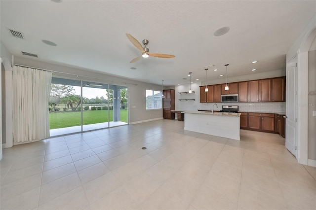 kitchen with hanging light fixtures, decorative backsplash, appliances with stainless steel finishes, brown cabinetry, and open floor plan